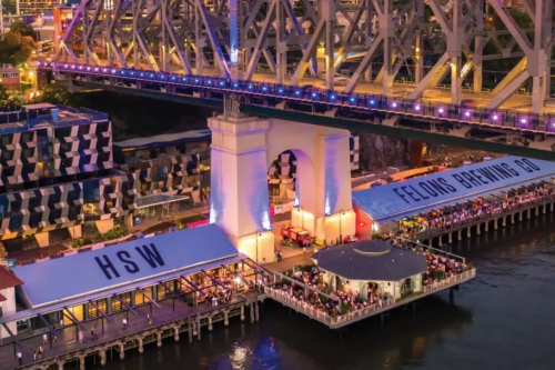 Aerial view of Howard Smith Wharves beneath the Story Bridge at dusk, with crowds dining along the Brisbane River.